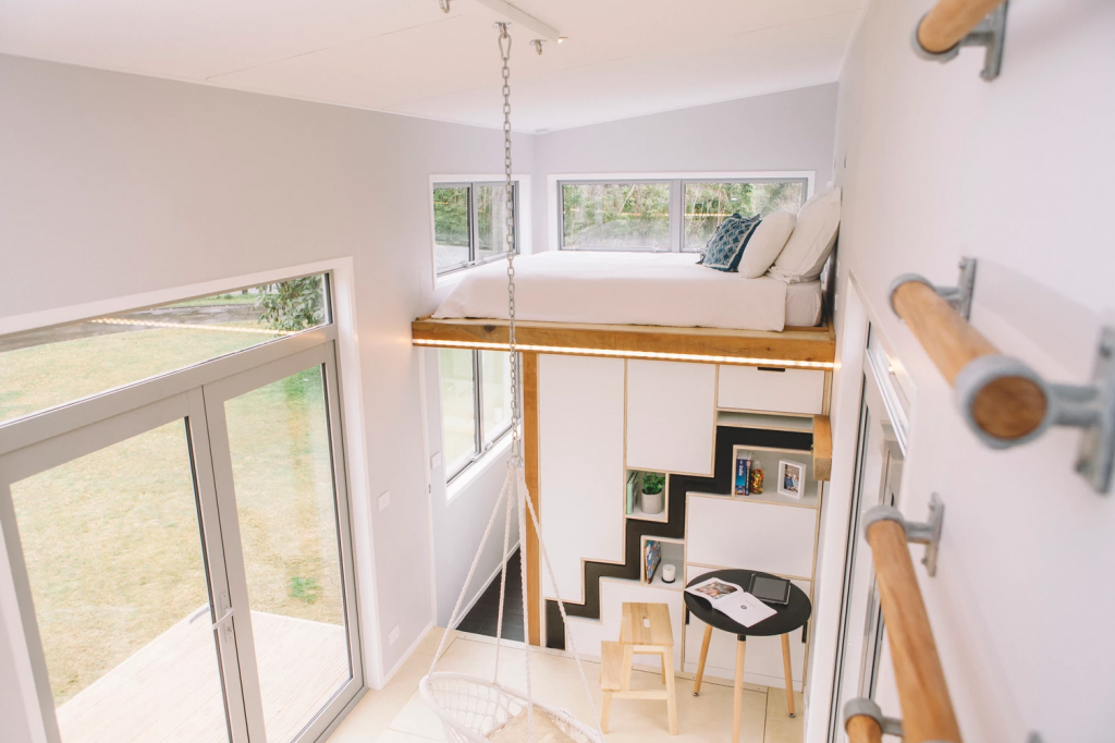 A view from the loft space above the kitchen, looking down to the floor space, the bathroom and the bedroom loft. Photo Credit: Build Tiny