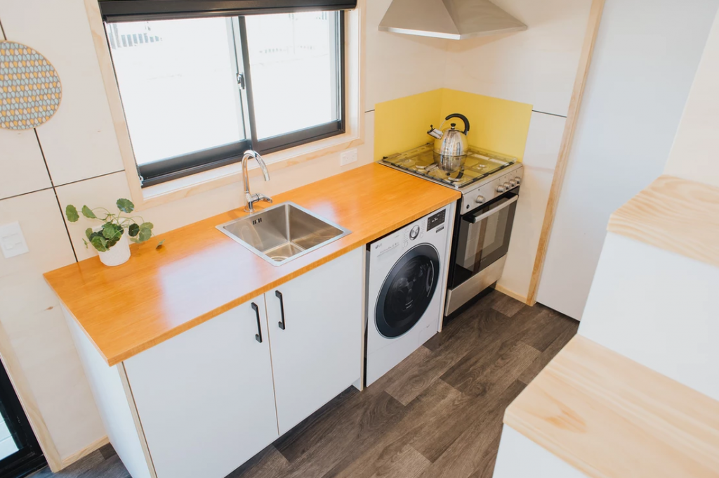 A long view of the kitchen in the Dreamweaver tiny house by Build Tiny. The end of the kitchen features a tiny house oven and cooktop.