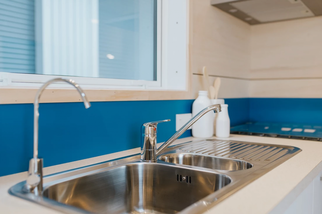 The tiny house kitchen sink in the Total Grace features two faucets and a drainboard built in.