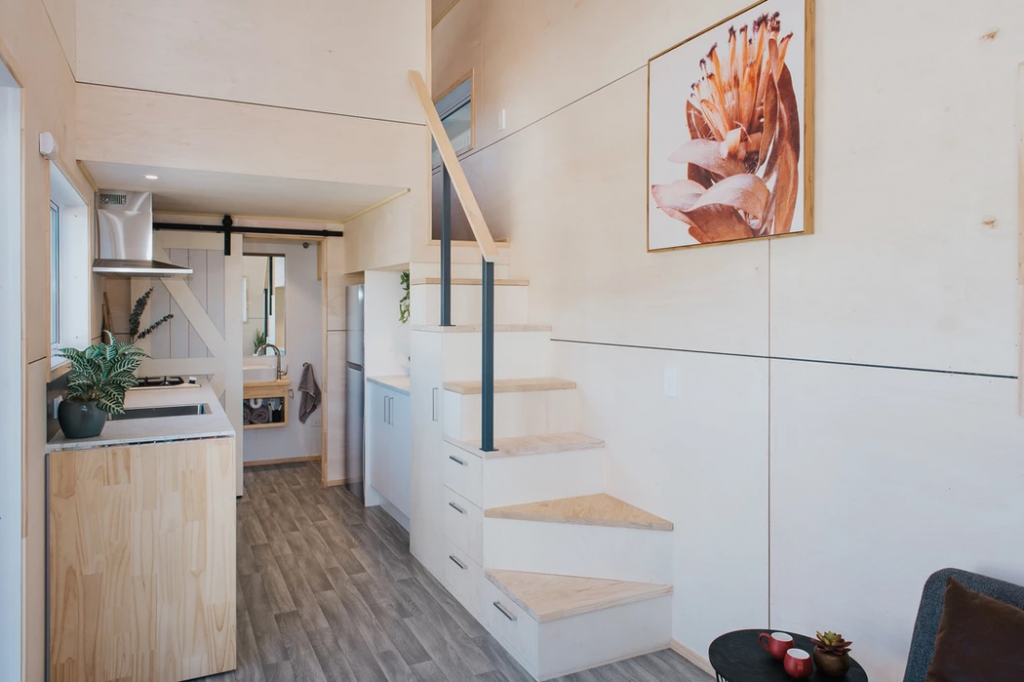 An image of the kitchen and stairs in the Purple Palace tiny house, which includes a view of the tiny house loft railing that leads to the upstairs.