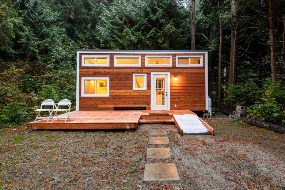 The exterior of the Robin tiny house with three double windows and three single windows, lit up with internal light.